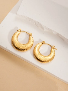 Detailed view of gold round earrings with swirling texture on white stone texture stand