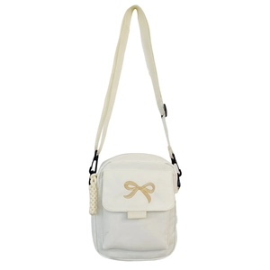 Detailed view of white crossbody bag featuring golden bow embroidery and side charm accessory