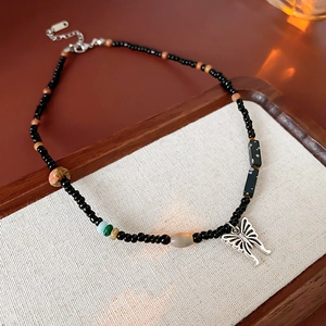Detail of a butterfly pendant necklace with ceramic beads on a rustic linen background