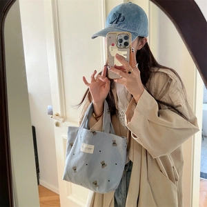 Detail of light blue corduroy handbag featuring cute bear embroidery and brand label