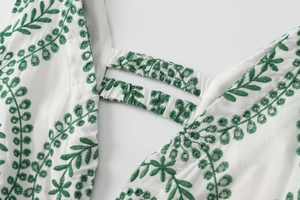 Detail eines weißen Bestickungskleids mit grünen Blattmustern und gesmokten Trägern