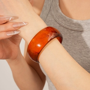 Close-up of a wide amber resin bangle with tortoiseshell patterns worn on a wrist