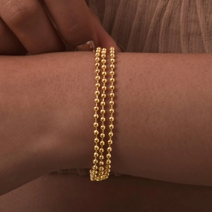Detailed view of triple-layered golden beaded snake chains worn on a woman's wrist