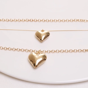 Detail of layered gold necklaces with two polished heart pendants on a white plate