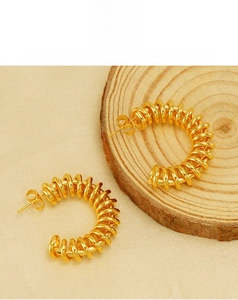 Detailed view of golden spiral spring C-shaped earrings on a natural wood surface