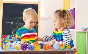 Kids playing with colorful mesh grape stress balls and crystal bead squeeze toys at a desk