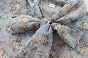 Détail du col d'un chemisier fleuri en mousseline avec nœud et texture légère