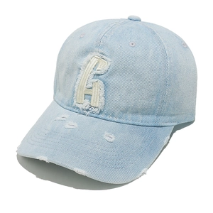 Macro detail of distressed light blue denim baseball cap with frayed white letter H embroidery