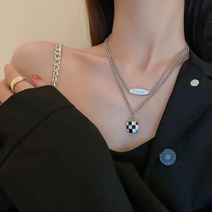Detail of layered silver necklaces with checkerboard pendant and Dream tag on a model