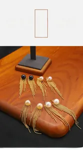 Detailed close-up of long gold tassel earrings with natural pearls on a wooden stand