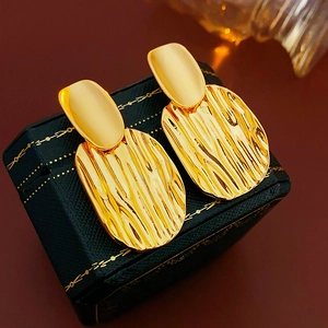 Gros plan de boucles d'oreilles dorées texturées dans un écrin de luxe marron foncé