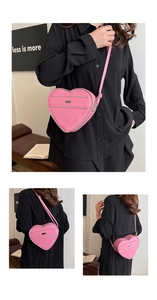 Detail view of a bright pink heart-shaped crossbody bag with metallic zipper and shoulder strap