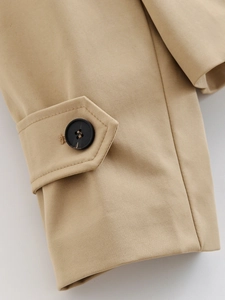 Detail of khaki trench coat cuff featuring a matte black button and strap craftsmanship