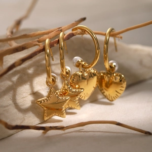 Detailed shot of gold heart and star earrings with pearls hanging on a natural branch