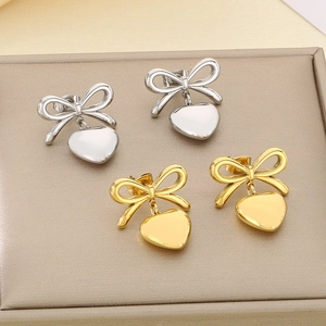 Elegant gold and silver bow heart earrings displayed on a beige jewelry tray