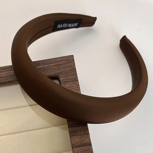 Detail of a dark brown satin headband with a handmade label on a padded display stand