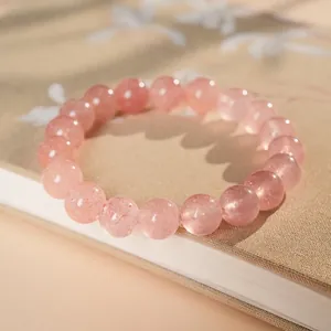 Pink strawberry quartz beaded bracelet on a book with artistic natural leaf shadows