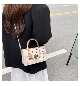 Detail of cream crossbody bag featuring cherry print, flower lock and woven handle