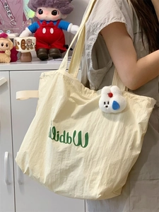 Detail of off-white canvas tote bag with green logo and plush bunny pendant