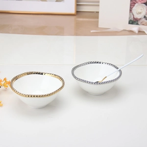 Detail view of white ceramic bowls with gold and silver bead rims and matching gold spoon