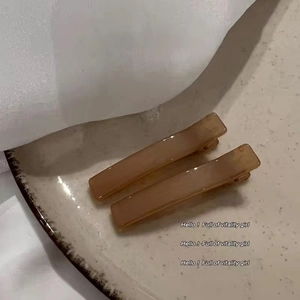 Macro view of two cream marble resin hair clips on a ceramic plate with soft lighting