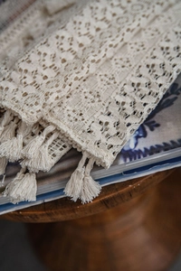 Close-up of beige crochet lace curtain fabric featuring floral hollow patterns and fringe