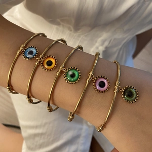 Dettaglio di bracciali aperti dorati con cinque ciondoli a forma di occhio di vari colori
