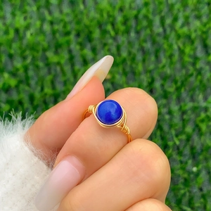 Macro detail of handmade wire wrapped gold ring featuring a round blue lapis gemstone