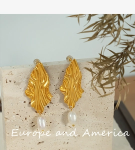 Detail of gold geometric earrings with freshwater pearls on a beige textured stone