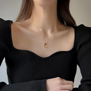 Dettaglio di una collana dorata minimalista con ciondolo ad anello e pietra nera