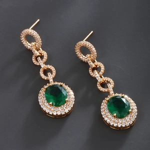 Close-up of vintage gold dangle earrings with green emerald stones and micro-pave crystals