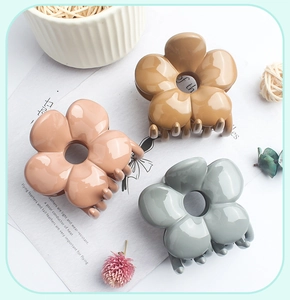 Three glossy flower hair claws in brown, khaki, and grey-blue shown on a decorative desk