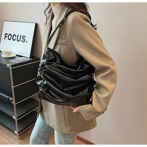 Dettaglio borsa tote in vernice nera lucida con trama plissettata su blazer color kaki