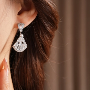 Close-up of fan-shaped silver earring with zircon inlay worn by model for elegant style