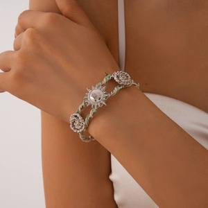 Detail of woven boho bracelet featuring silver sun and rose flower charms on wrist