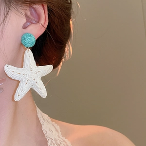 Detailed view of woven raffia starfish earrings in turquoise and white for summer style