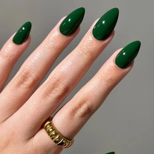 Gros plan d'ongles amande vert foncé brillants avec un anneau doré ondulé élégant en accessoire