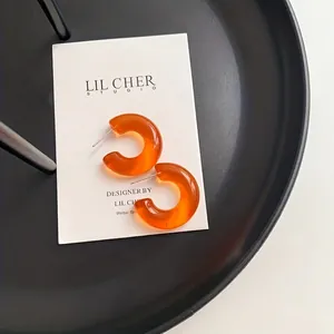 Transparent orange C-shaped jelly resin earrings on a white card and black tray