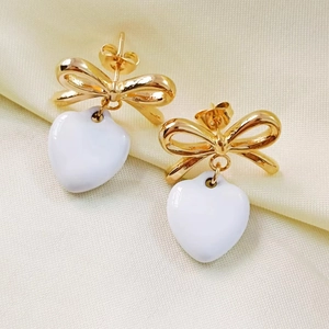 Detail of elegant gold bow earrings with a smooth white heart-shaped pendant charm