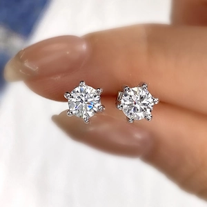 Close-up of a silver six-prong moissanite stud earring held between fingers for scale