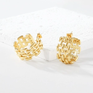 Detailed close-up of gold hollow earrings with woven pattern on textured stone base