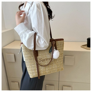 Detail of straw tote bag with brown faux leather straps and embroidered lettering