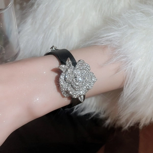 Detail eines Kristallrosen-Anhängers an einem schwarzen Lederarmband am Handgelenk
