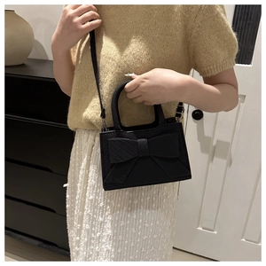 Detail of black crossbody bag with bow decoration and lychee leather texture on a model