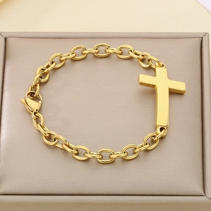 Detail of a gold O-chain bracelet with a smooth cross pendant in a beige jewelry box
