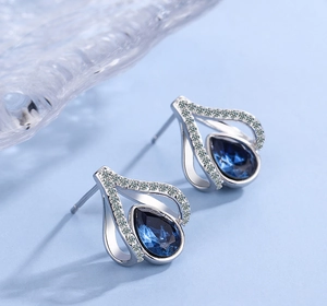 Detailed macro view of silver water drop earrings with dark blue crystal and zircons