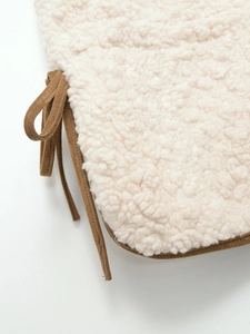 Detail of cream sherpa cushion featuring brown suede edging and tie-on straps