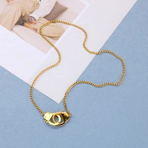 Detailed close-up of golden stainless steel handcuff pendant necklace on a textured background