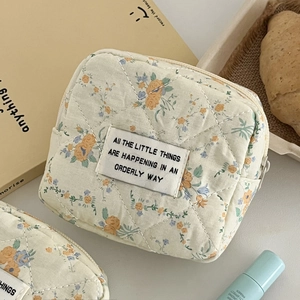 Close-up of beige quilted floral pouch with orderly text patch and smooth zipper closure