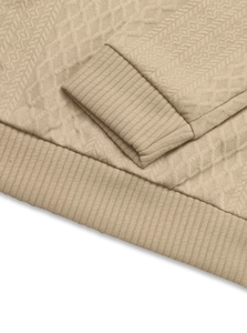Dettaglio della trama trapuntata a rombi e del polsino a coste sulla felpa beige